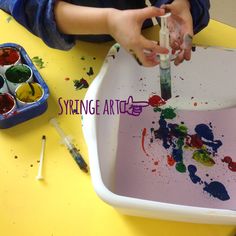 a child is painting with paint in a white container on a yellow table next to other paints