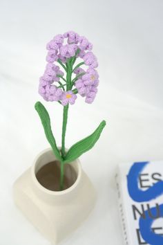 a small white vase with purple flowers in it next to an e s news book