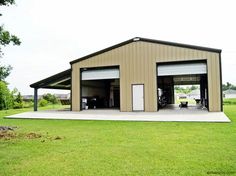 a large garage with two cars parked in front of it on top of a grass covered field