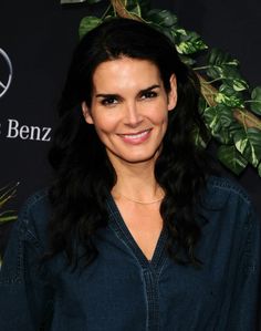 a woman with long black hair smiling at the camera and wearing a dark blue shirt