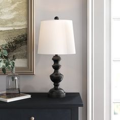 a lamp on a black dresser next to a painting and a bookcase with books