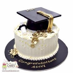 a graduation cake is decorated with white frosting and gold decorations, including a black cap and tassel