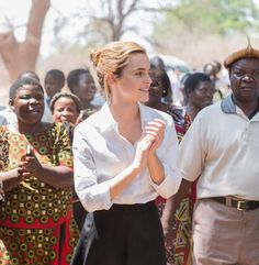 a woman in white shirt and black pants standing next to other people with hands together