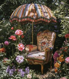 an old chair is sitting in the middle of flowers and has an umbrella over it