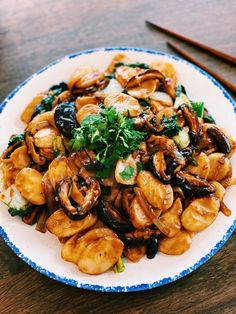 a white plate topped with lots of food on top of a wooden table next to chopsticks