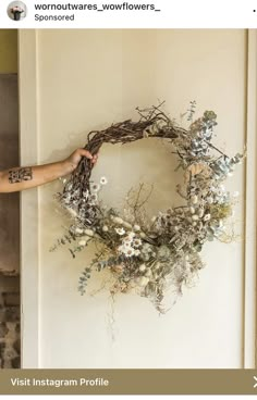 a person is holding a wreath on the wall with flowers and vines attached to it