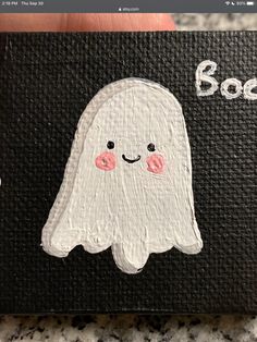 a hand holding up a painted ghost on a black background with the word boo written in white