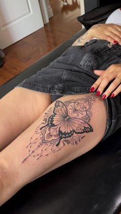 a woman sitting on top of a black couch with a butterfly tattoo on her leg