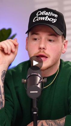 a man sitting in front of a microphone with tattoos on his arm and wearing a black hat