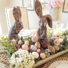 two wooden rabbits sitting on top of a table with flowers and eggs in front of them