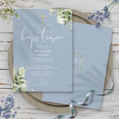 two blue wedding cards with white flowers and greenery on them, sitting next to each other