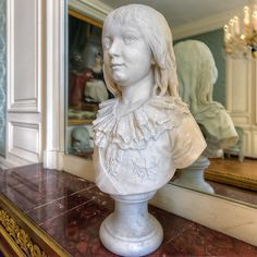 a white busturine sitting on top of a marble table next to a mirror