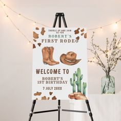 a welcome sign with cowboy boots on it next to a potted plant and string lights