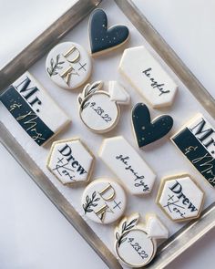 decorated cookies are displayed in a metal tray on a white tablecloth with black and gold accents