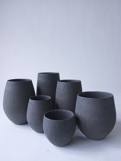 five gray vases are lined up in a row on a white surface, with one empty