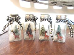 four glass jars with christmas trees and deer in them sitting on a table next to a window