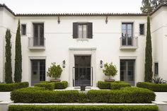 a white house with hedges in front of it and potted plants on the side