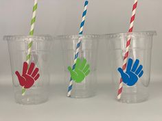 three plastic cups with different colored straws in them and hand prints on the lids