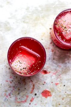 two red glasses filled with liquid and sprinkles on top of a table