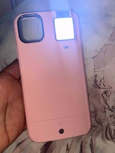 a hand holding a pink cell phone with a light on it's back cover