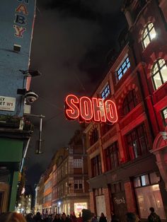 people are walking down the street in front of some tall buildings with neon lights on them