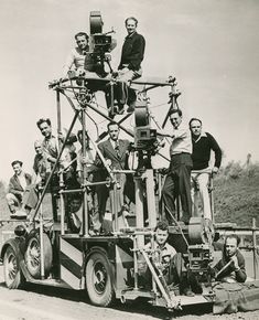 a group of men standing on the back of a truck in front of a camera