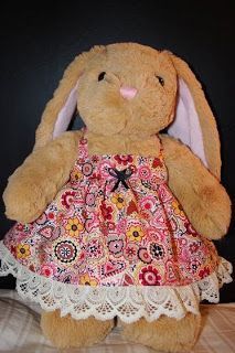 a stuffed rabbit in a dress sitting on a wooden table next to a black wall