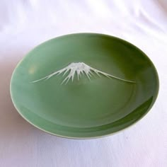 a green plate with a white mountain painted on the front and side, sitting on a white tablecloth