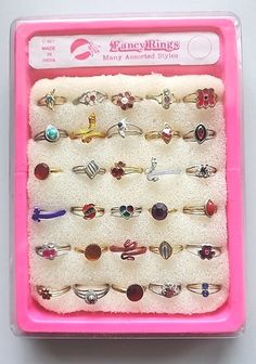 a pink plastic box filled with lots of different types of rings on top of a white surface