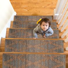 a toddler is crawling down the stairs on carpeted flooring in front of wooden banisters