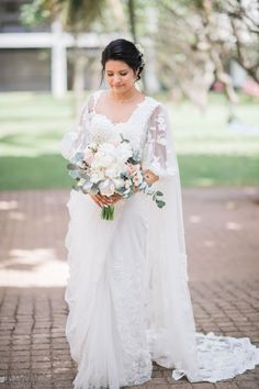 a woman in a wedding dress holding a bouquet and looking down at her gown while standing on a brick walkway