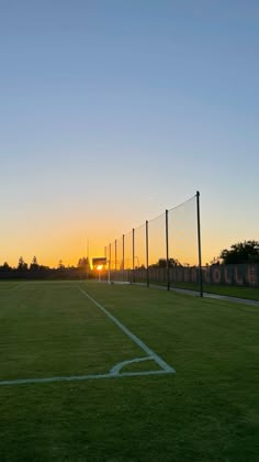 the sun is setting over a soccer field with goal posts in the foreground and trees on the other side