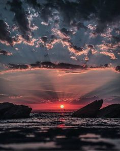 the sun is setting over some rocks in the ocean with water and clouds above it