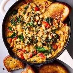 a pan filled with pasta and spinach on top of a table next to slices of bread