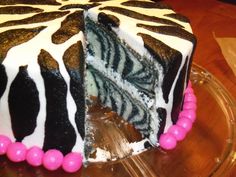 a zebra print cake with pink and white frosting on a glass platter that is half eaten