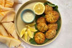 a plate filled with crab cakes and lemon wedges next to a bowl of ranch dressing