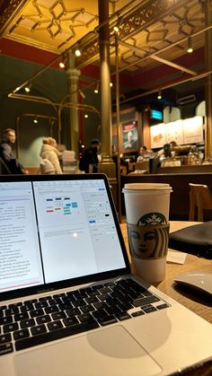 a laptop computer sitting on top of a wooden table next to a cup of coffee