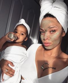 a woman is holding a baby while wearing a towel on her head and she has a face mask on