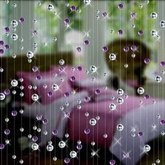 rain drops falling down on a window with a woman in the background behind it,