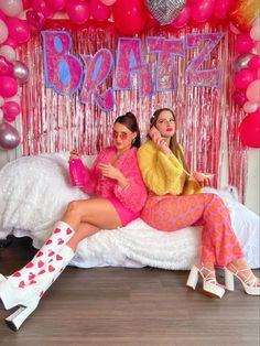 two women sitting on a bed in front of balloons and streamers with the word booze