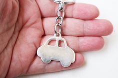 a hand holding a silver key chain with a small car charm on it's side