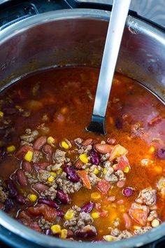 a pot filled with chili and beans on top of a stove next to a spoon