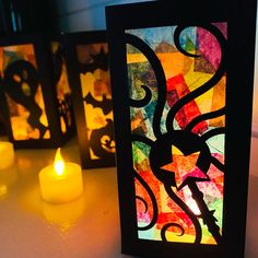 three lit candles sitting on top of a table next to paper cutouts with designs