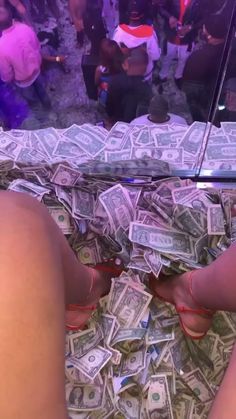 a person sitting on top of a bed covered in lots of dollar bills and wearing red shoes