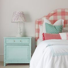 a pink and white checkered headboard next to a blue nightstand with a lamp on it