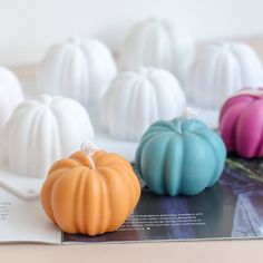 small pumpkin shaped candles sitting on top of a magazine next to each other, all in different colors