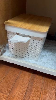 a white plastic basket sitting on top of a wooden floor next to a cutting board