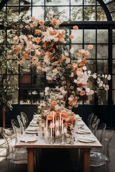 a long table with candles and flowers on it in front of an arched glass window