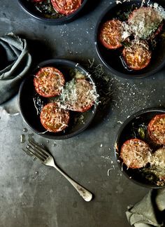 four small black bowls filled with tomatoes and parmesan cheese on top of a table