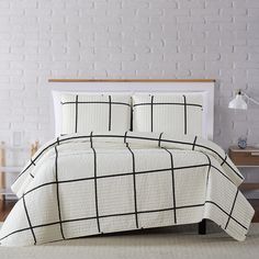 a bed with white and black bedspread in a room next to a chair